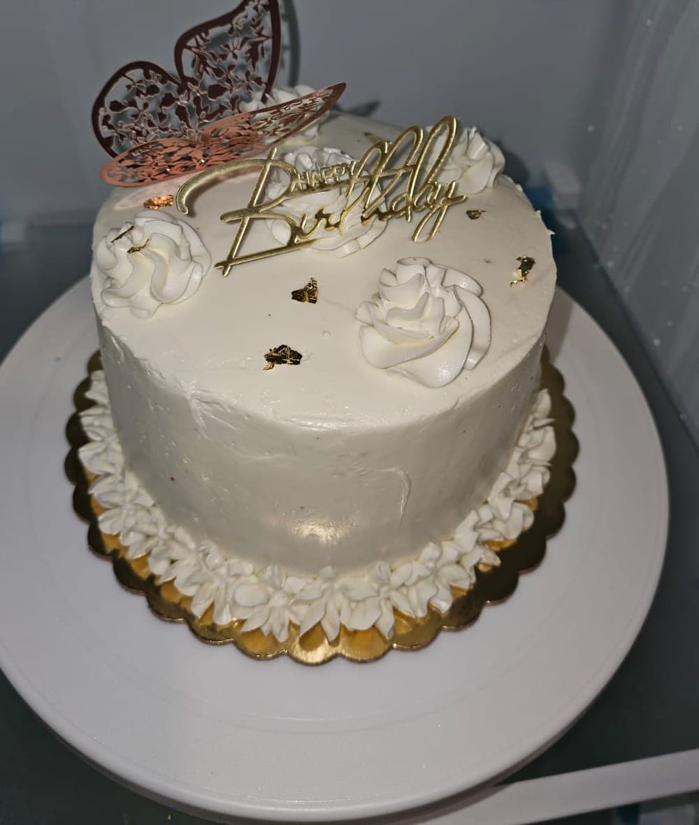 White buttercream birthday cake with piped rosettes, gold leaf and a rose-gold filigree butterfly.