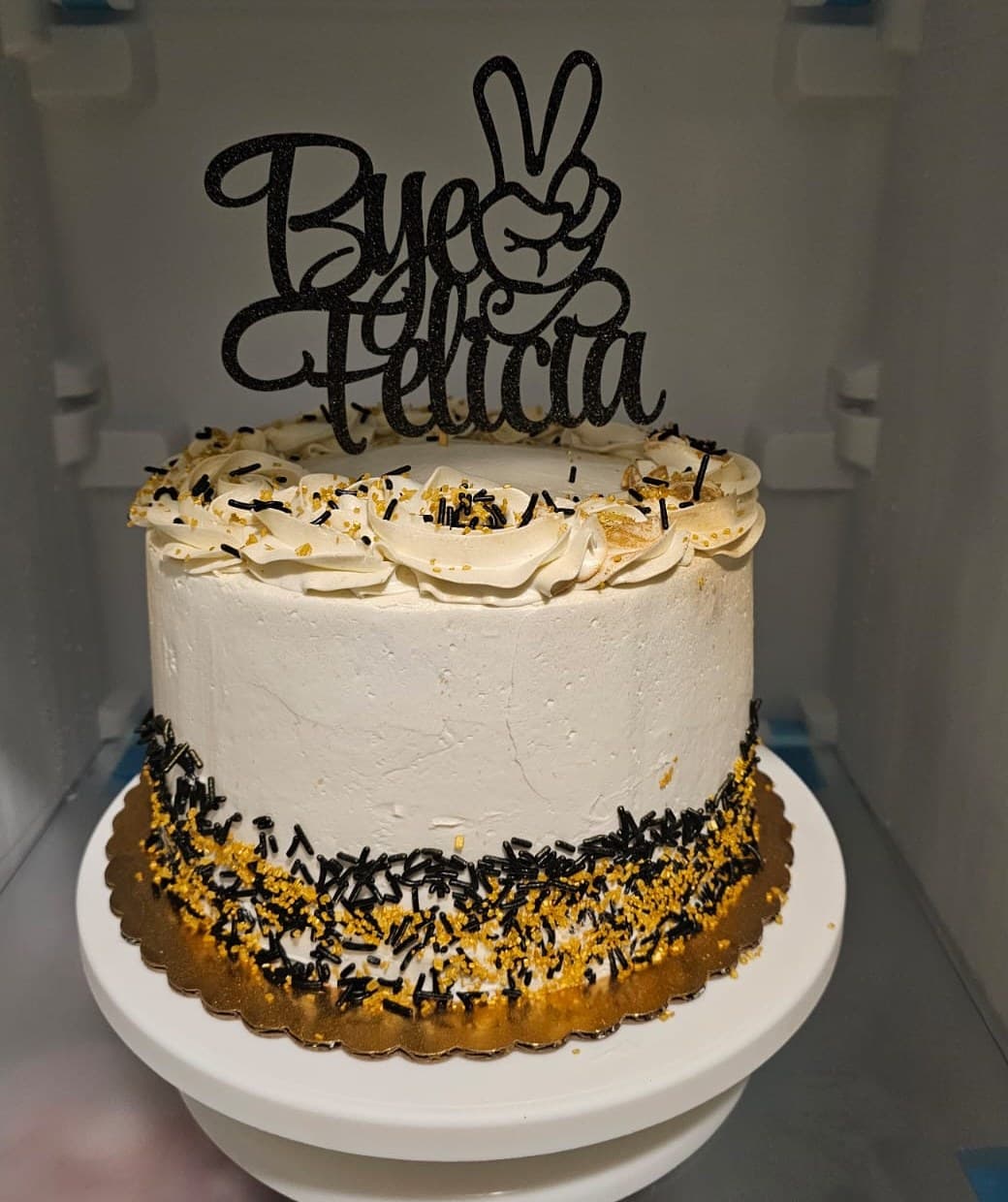 White cake with black and gold sprinkles and a “Bye Felicia” topper.
