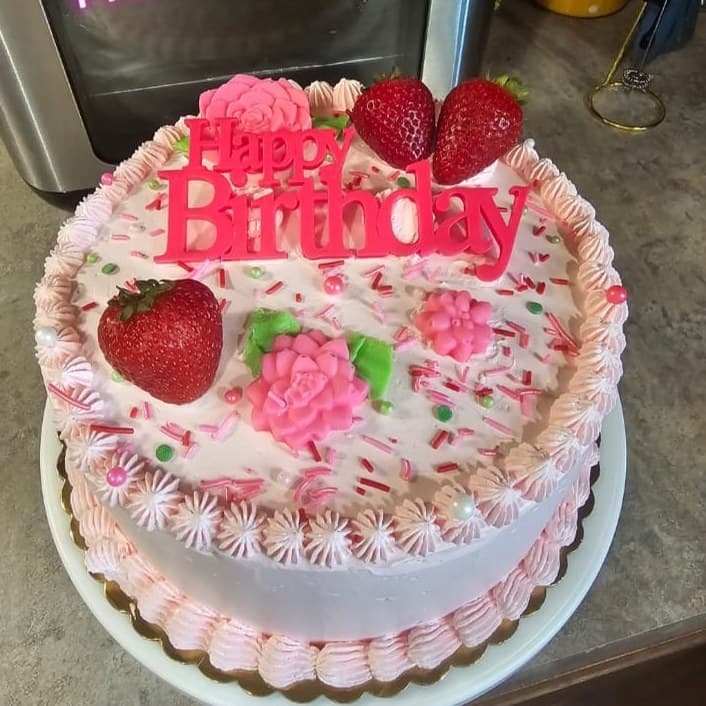 Pink-and-white birthday cake with fresh strawberries, sugar flowers and sprinkles.